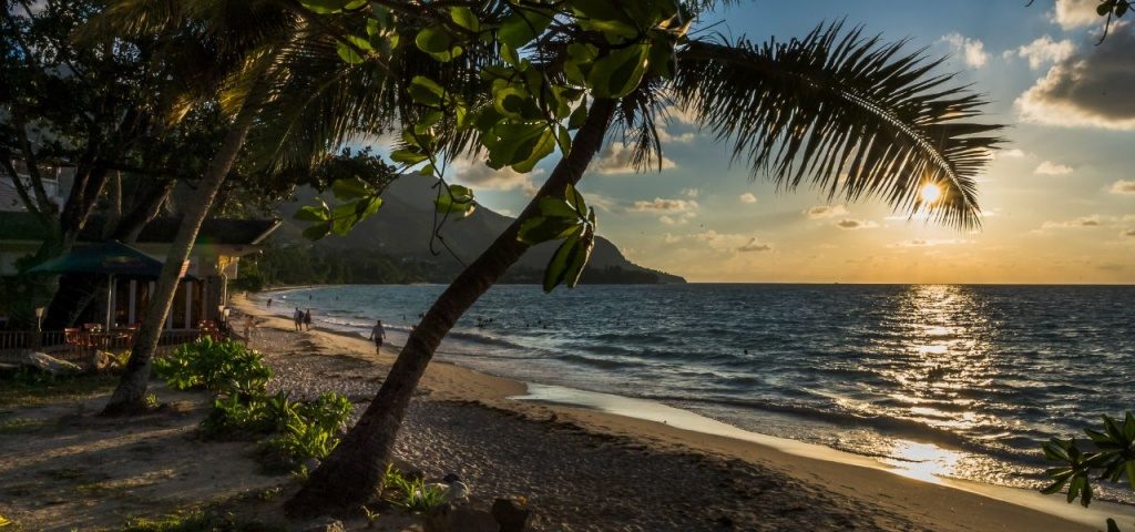 Długi łuk plaży Beau Vallon o zachodzie słońca z łodziami, Mahé